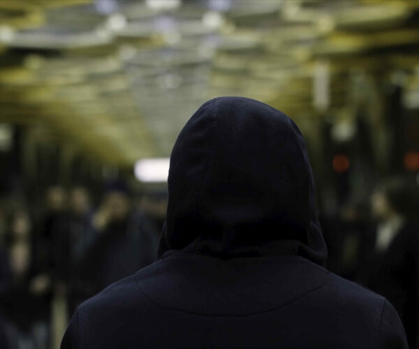 Rear view of a man with a dark blue hoodie on standing in front of a crowd at the station, resistance concept. Close up for man back in front of many people in subway.